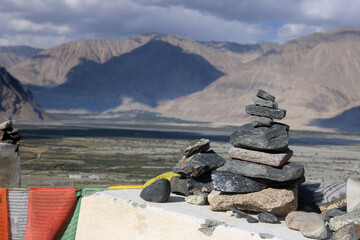 An image of a stacked rock cairn, which is a common sight in the mountainous region of Ladakh, India. The stacked rocks are a traditional wayfinding marker or a spiritual offering in many cultures.