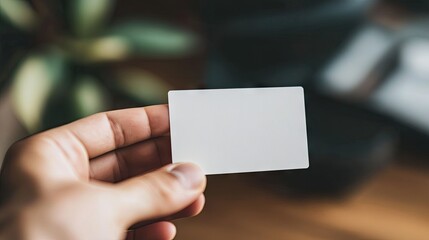 Obraz premium Hand Holding Blank White Card Against Blurred Plant Background with Soft Lighting for Business and Identity Concepts in Stock Photography