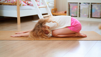 Young girl doing child's pose yoga on floor mat