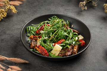 Flavorful arugula salad mixed with tender beef slices sundried tomatoes parmesan and herbs on plate