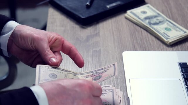 Close-up of hands counting money in front of laptop on table, businessman counting his profit