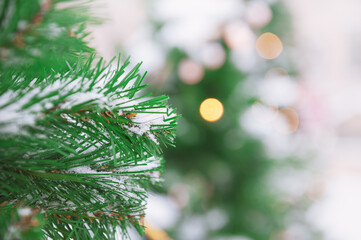 Snow-covered branches of a Christmas tree glow with festive lights, creating a magical winter scene