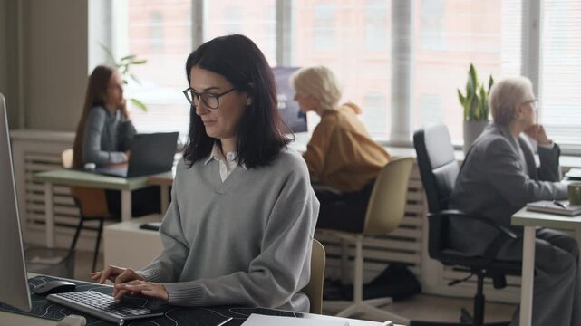 Medium shot of motivated Caucasian female programmers of different age sitting at desks in front of computers in open space office, working together in female IT company