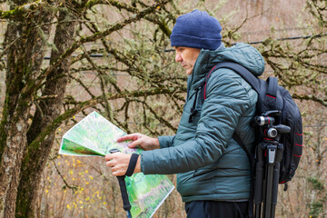 Exploring nature with a map in hand, a hiker pauses in a quiet forest trail while analyzing the lush surroundings during a chilly autumn afternoon