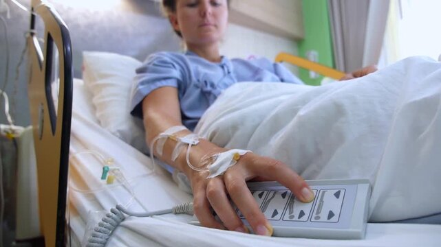 Female patient with an iv drip in her hand resting in a hospital bed and pressing a button on the remote control to adjust her position for better comfort during medical treatment