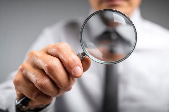 A man in a shirt and tie holds a magnifying glass up close to the viewer