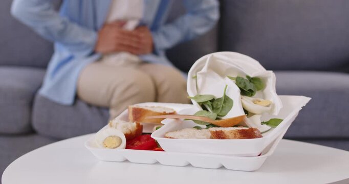 Stomach pain after fastfood takeout causes indigestion. A seated person clutches belly beside a takeaway box, implying food poisoning with cramps, diarrhea and nausea. Keep food safety in mind.