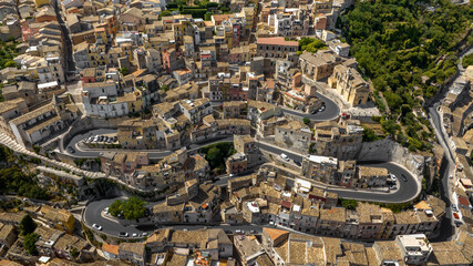 Fototapeta premium Aerial view of a paved road through an Italian hilltop village nestled between the mountains. This is the historic center of Ragusa Ibla, Sicily, Italy.