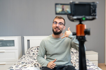 Young man creating new content for his social media channel, talking to a camera on a tripod in a bedroom setting