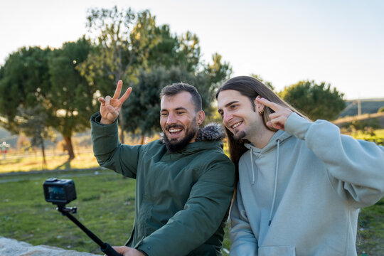 Two male friends recording a video outdoors, showing happiness and peace signs while sharing moments on a vlog