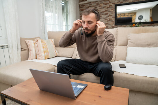 Man setting up headset, preparing for remote video conference call from home office couch, modern telecommuting lifestyle