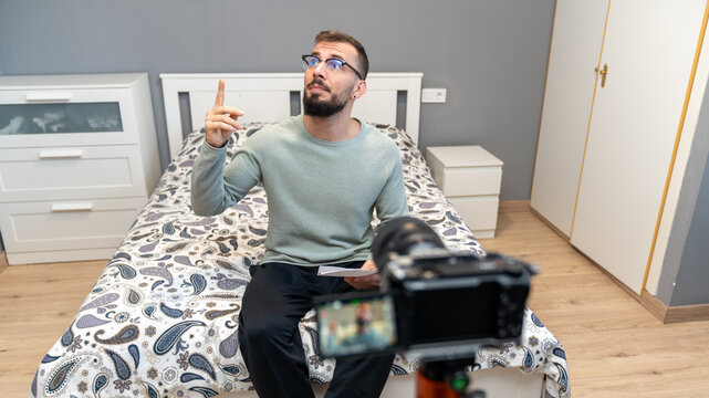 Young man vlogging from home, explaining content to camera, creating online video for social media streaming