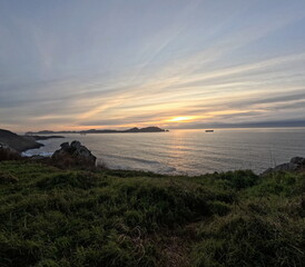 Obraz premium Golden sunset over the Atlantic Ocean from Cabo Home, Galicia, Spain The Cíes Islands silhouette in the background and a cargo ship sailing under a sky filled with soft clouds 