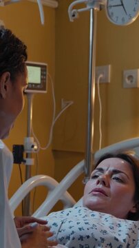 black doctor comforts white patient bedside holding hand with infusion pole and monitor in warm yellow room, clinical gown, empathetic expression, quiet reassurance during recovery