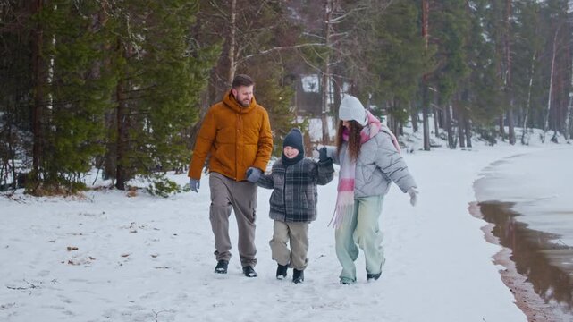 Full length slowmo shot of happy Caucasian family of three walking together on path in snowy forest path enjoying winter nature