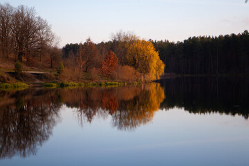 Autumn trees reflected in calm river at sunset
