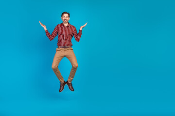 Fototapeta premium Young stylish man jumps in red striped shirt and khaki pants against a blue background perfect for lifestyle fashion advertising