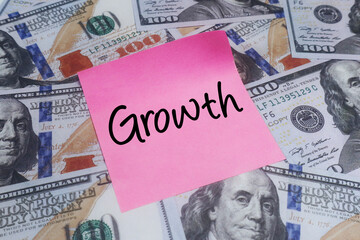 Growth concept on a pink sticky note placed atop a scattered bed of US hundred dollar bills, symbolizing financial expansion, increasing wealth, and successful investment strategies in business