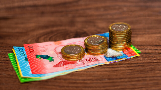 Stacks of 500 colones coins and colorful Costa Rican banknotes on a wooden surface, symbolizing money, savings, and financial growth.