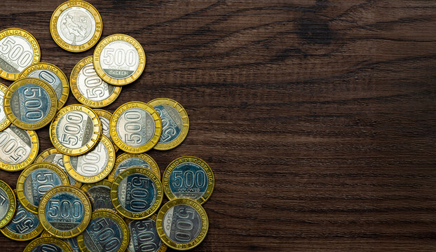 Multiple 500 colones coins from Costa Rica scattered on a dark wooden surface, representing currency, economy, and financial concepts.