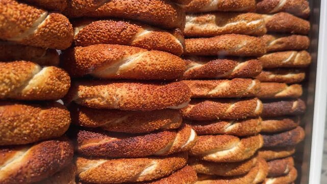 Close up motion along freshly baked simit piled high in a glass-fronted street simit cart