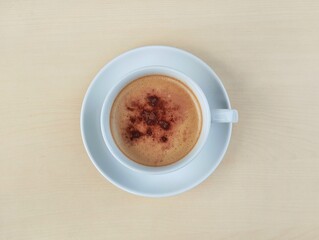 Cappuccino coffee in white cup with wooden table background. Flat lay view 