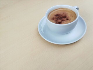 Cappuccino coffee in white cup with wooden table background. High angle view. Copy space 
