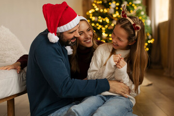 Family sharing joyful moment in living room, smiling and playing together, Christmas tree, adorned...