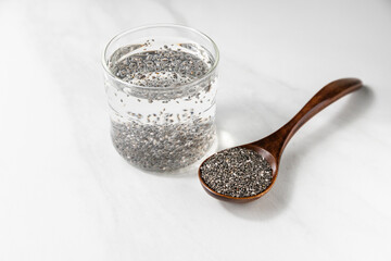 Glass of hydrated chia seeds and wooden spoon with dry chia on light marble background