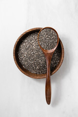 Top view of chia seeds in a wooden bowl with a spoon on a light marble background, minimal healthy food concept.