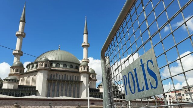 Police barrier in front of Taksim square mosque with twin minarets under bright blue sky in central city area
