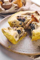 Quiche with chanterelles, oyster mushrooms, champignons, and cheese, piece of quiche cut off for eating on plate.