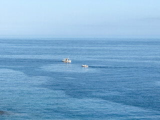 Obraz premium Small fishing boats crossing calm blue water under clear morning sky, viewed from distance image