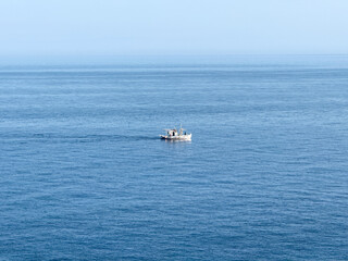 Solitary fishing boat upon calm blue sea at morning, small vessel leaving gentle wake within tranquil water