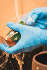 close-up of female hands wearing protective gloves while washing dishes under running water. A simple everyday household scene that conveys cleanliness, care, and routine home maintenance.