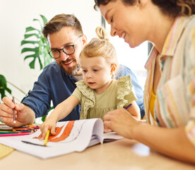 Portrait of a little girl and mother and father or teacher coloring a book in classroom or at home. Education and development concepts