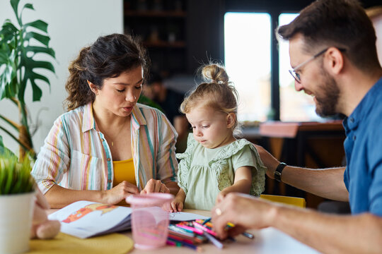 Portrait of a little girl and mother and father or teacher coloring a book in classroom or at home. Education and development concepts - Powered by Adobe