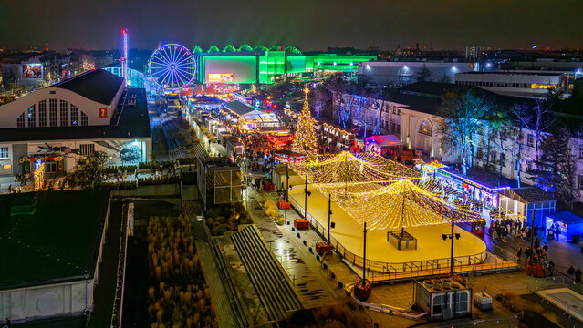 Night drone view of the Poznan MTP Christmas market with illuminated ice rink, ferris wheel, Christmas tree and festive stalls across the grounds