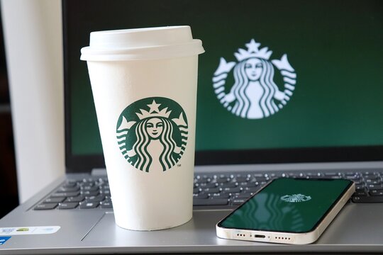Salvador, Brazil - November 20, 2025: Starbucks Coffee Cup and smartphone in front of laptop with Starbucks Logo. 