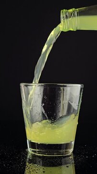 stream of yellow soda pouring from a bottle into a glass on a dark background for beverage themes, bar content, drinks, tasting, party or summer refreshment concepts
