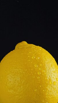 Yellow lemon with water drops. Vertical video of a whole ripe yellow lemon on a dark black background with visible water drops on the textured citrus peel