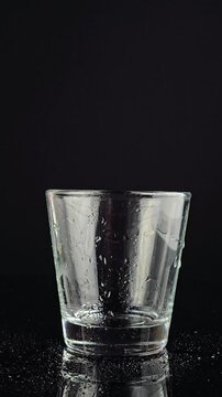 Hand in glove adjusting and placing a wet empty glass on a dark background in vertical video. person&rsquo;s gloved hand aligning a clean wet glass on a dark surface