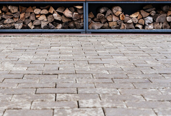 Wooden logs stacked neatly in metal racks on a paved surface. The scene showcases a rustic storage solution for firewood, copy space