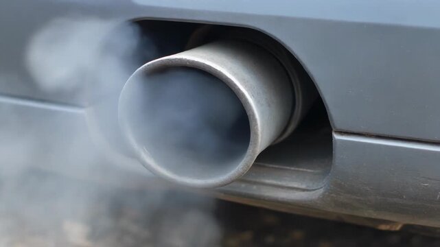 Close-up of exhaust fumes emitting from the exhaust pipe of a generic grey passenger vehicle emitting exhaust gases.