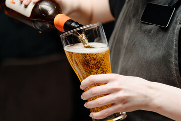 bartender pours light beer into large beer mug for customer at bar, close-up view of hand holding mug and bottle