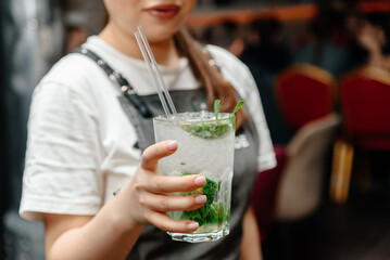 mojito cocktail in glass with mint and ice cubes and straw in waitress hand, nightlife concept