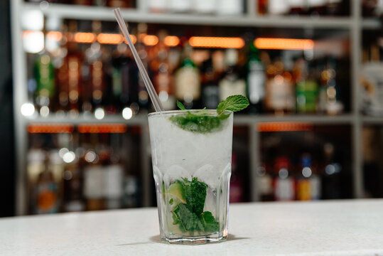 mojito cocktail in glass with mint and ice cubes and straw on bar counter, nightlife concept