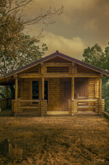 Close-up view of a charming traditional log cabin with warm golden hour lighting. Detailed shot showing notched log walls, wooden front porch with railings, windows and doors. Cozy rustic wooden house