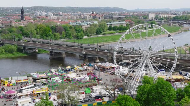 A drone captures the fair at Dresden&rsquo;s Ostpark: a large Ferris wheel, colorful rides, and visitors by the Elbe, with the city and its bridges in the background.