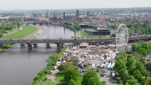A drone captures the fair at Dresden&rsquo;s Ostpark from above. The Ferris wheel, colorful booths, and the Elbe dominate the view, with Dresden&rsquo;s historic old town rising in the background.